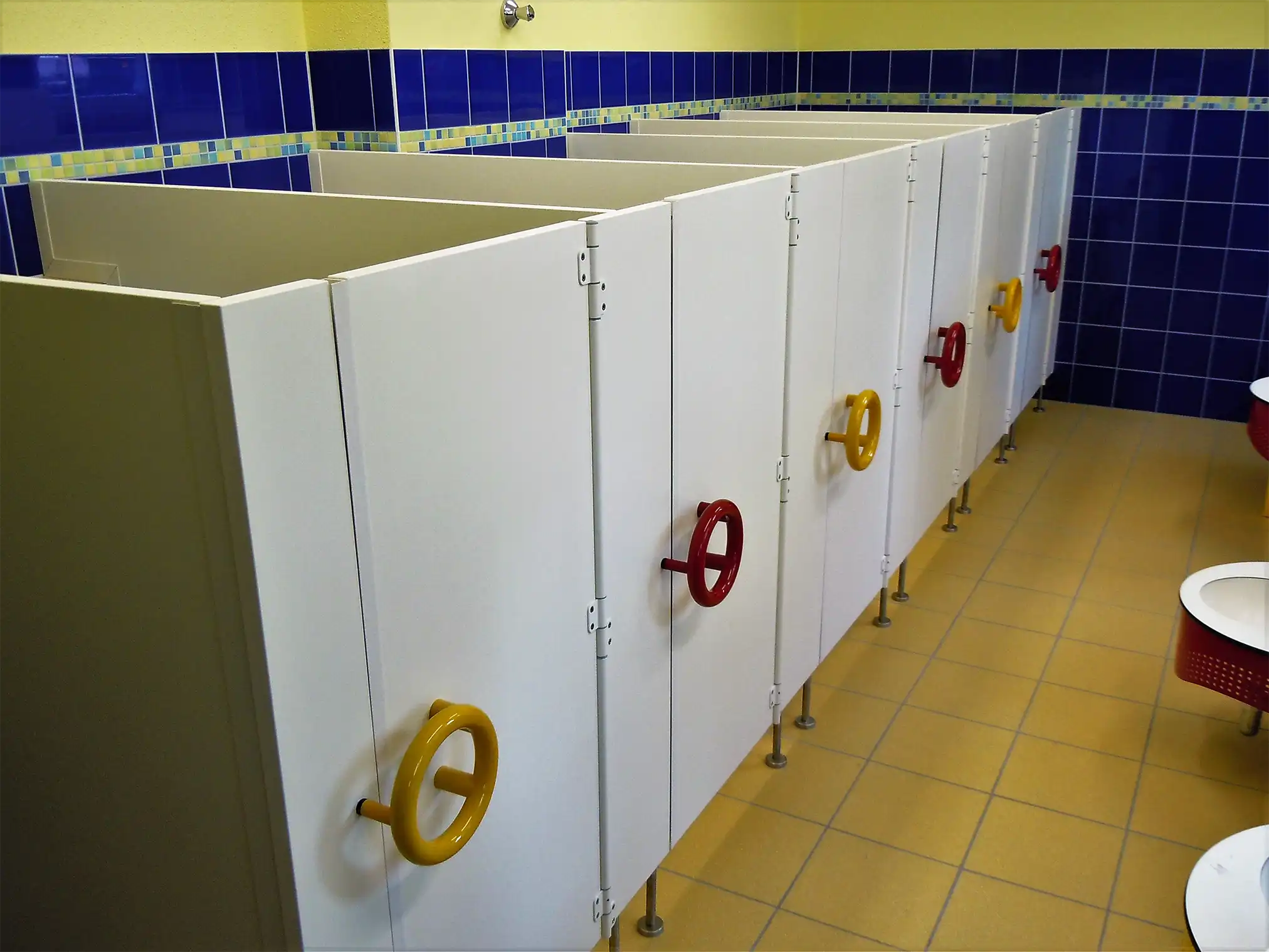 Weiße Kindergarten-WC-Trennwände mit bunten Ringgriffen in einer Kita